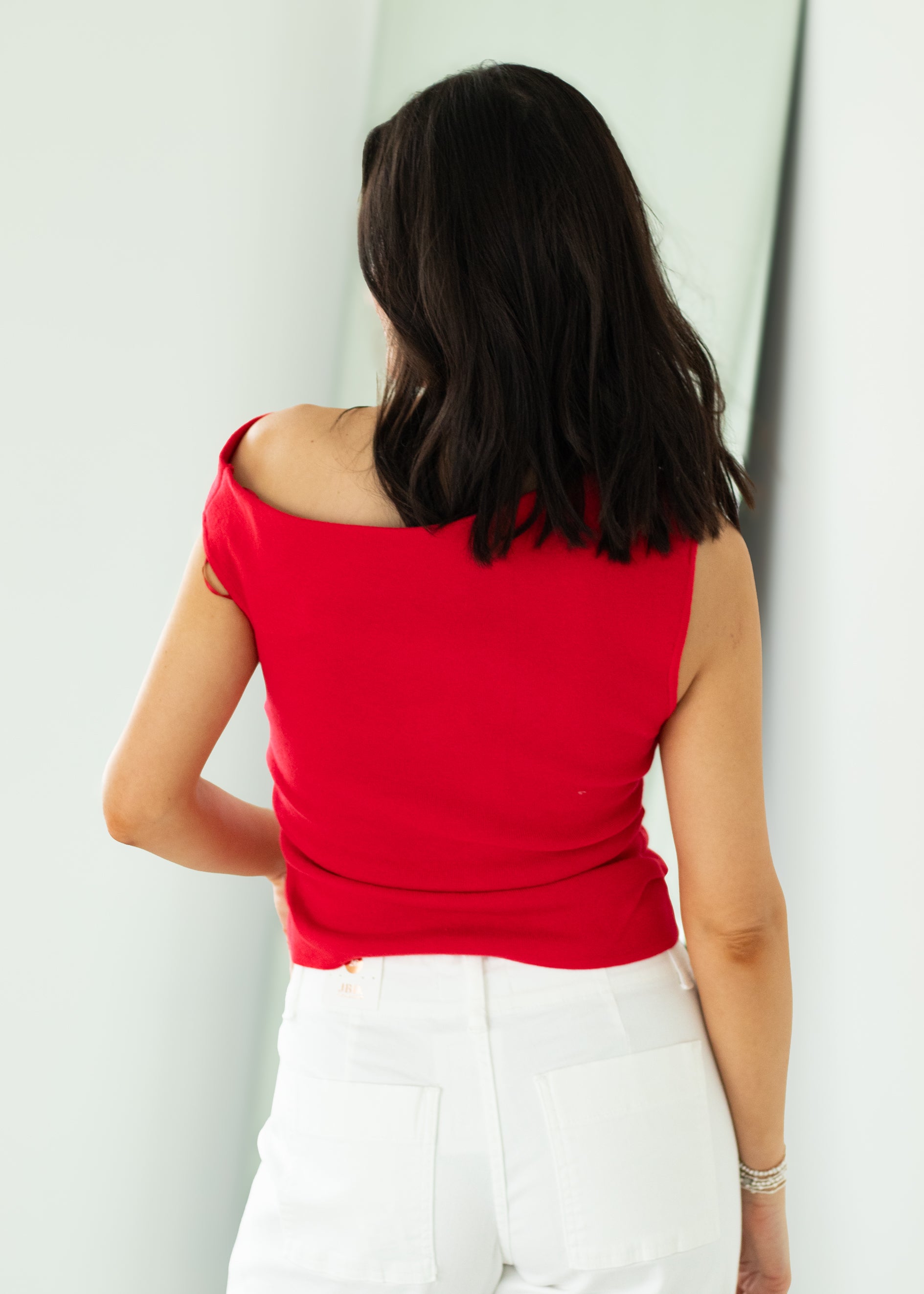 Woman wearing a red top and white pants against a light background