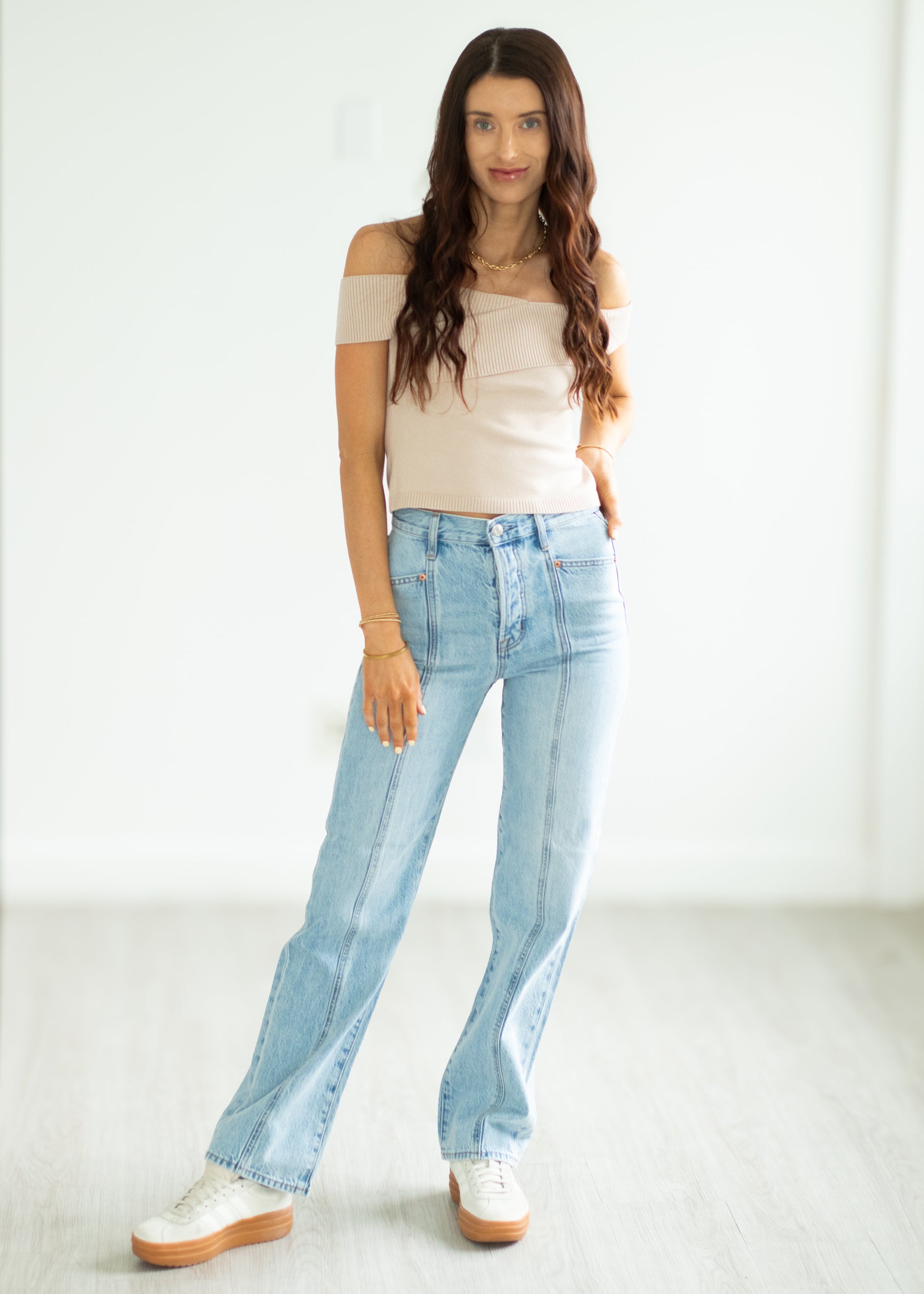 Woman wearing a beige top and light blue jeans on a white background