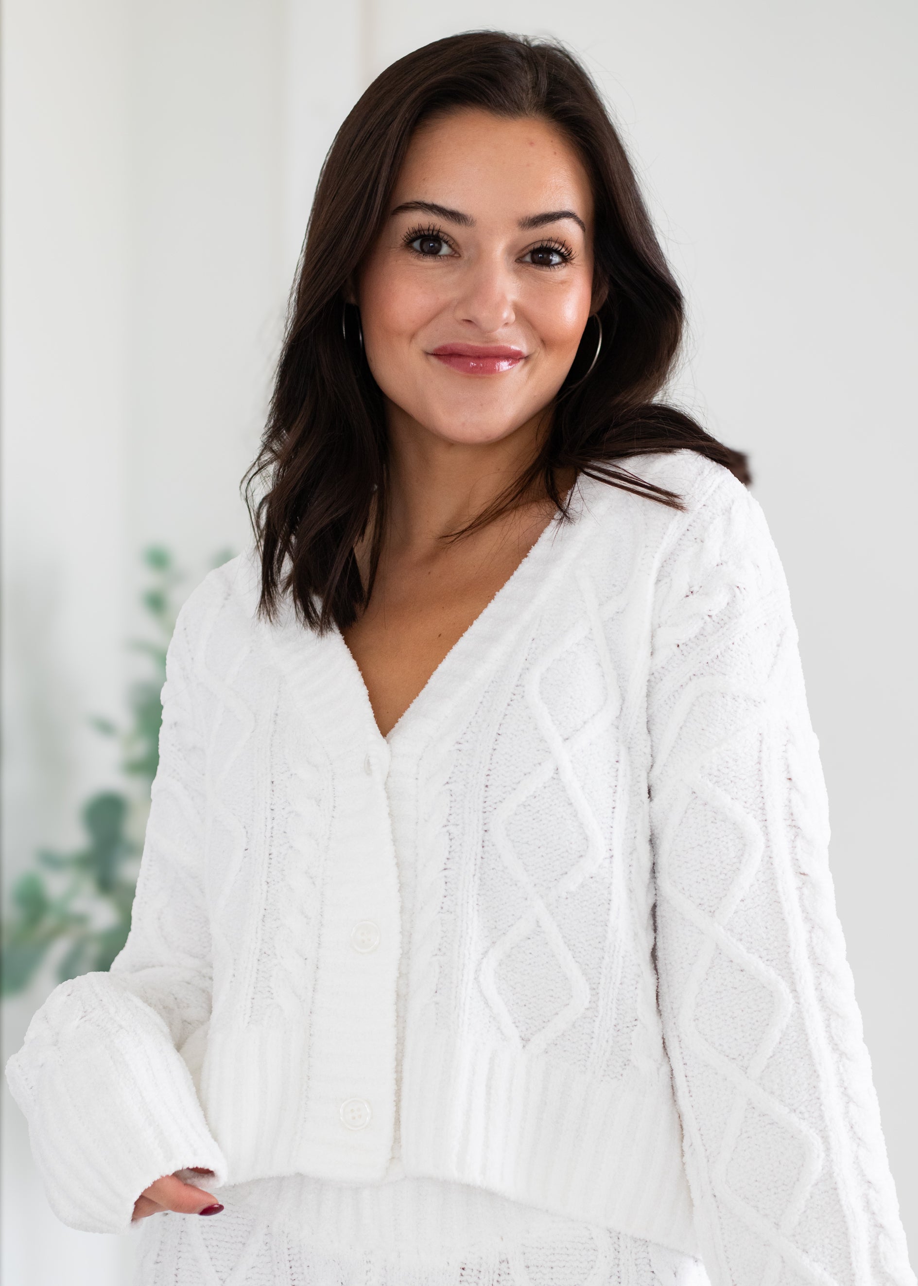 Woman wearing a white cable knit sweater against a light background