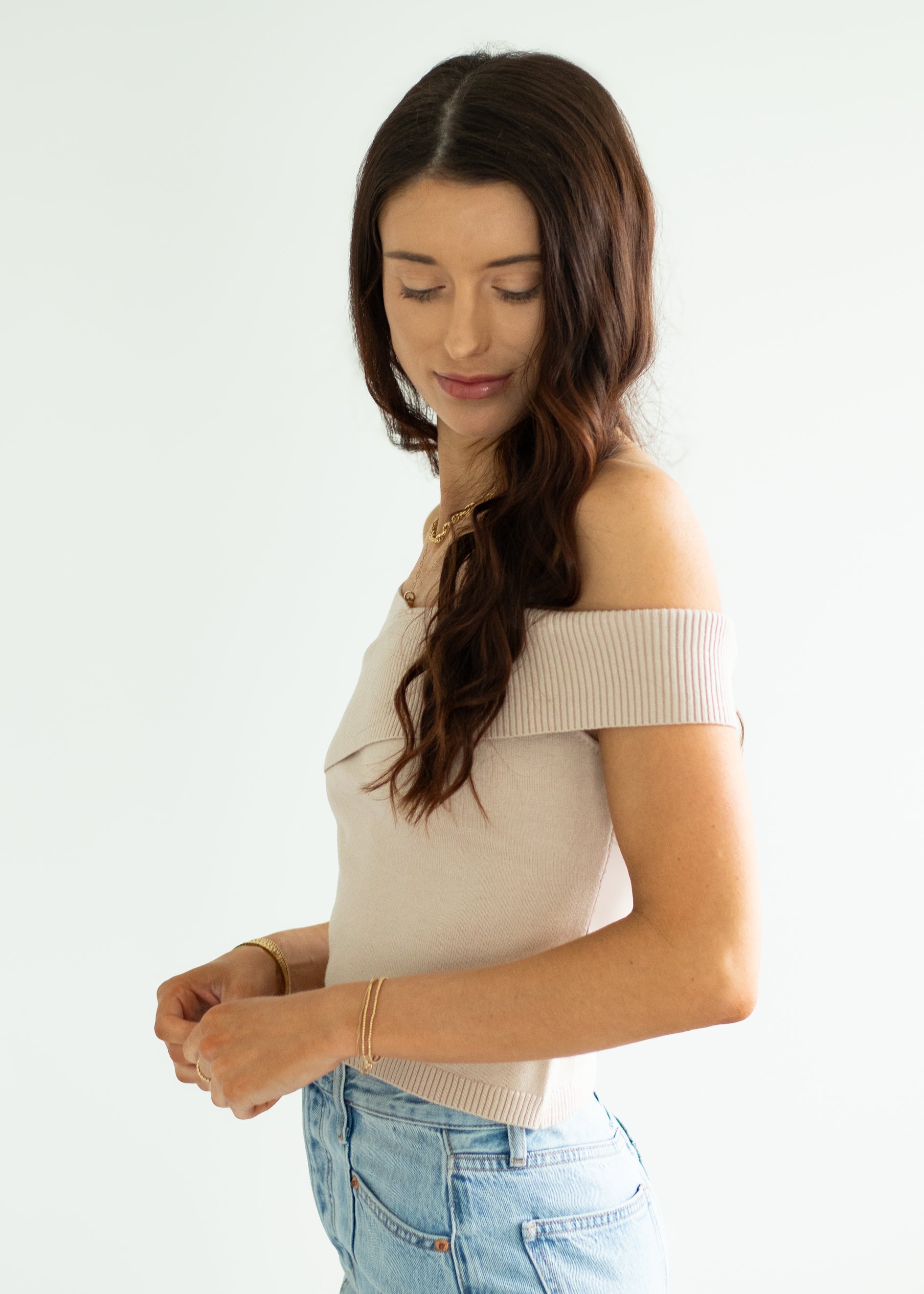 Woman wearing a beige off-shoulder top and blue jeans on a white background