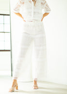 Person wearing a white lace outfit with high-waisted pants and a button-up top.