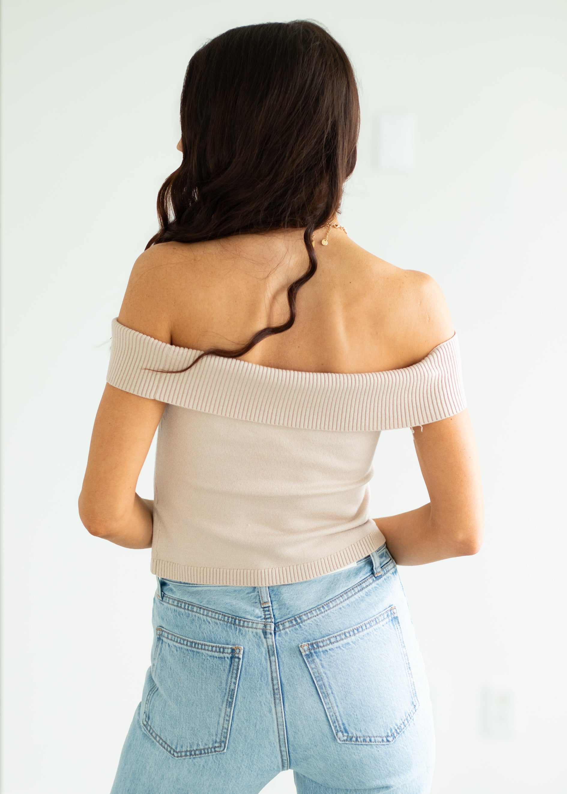 Woman wearing a beige off-shoulder top and light blue jeans against a white background