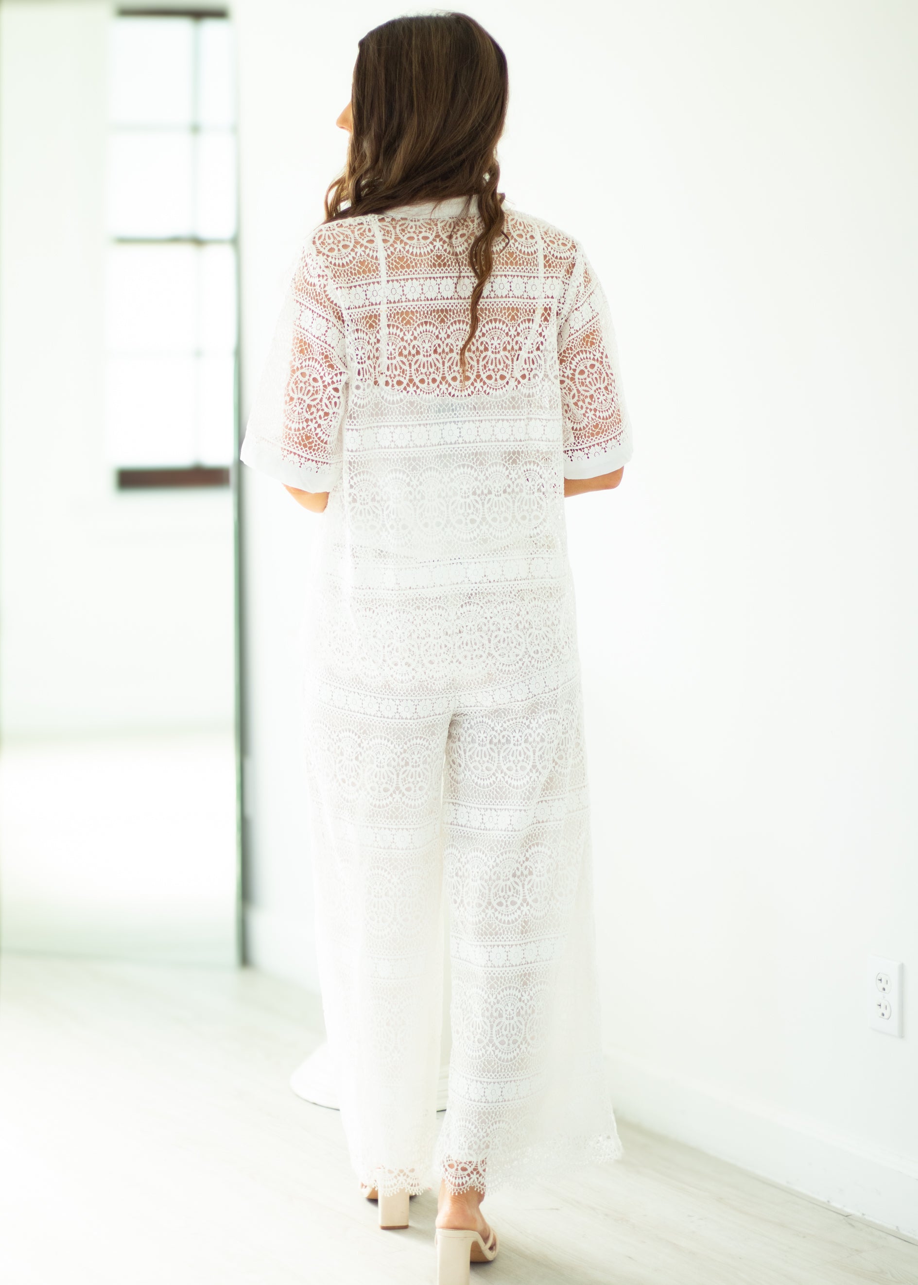 Woman wearing a white lace outfit standing in a minimalistic room.