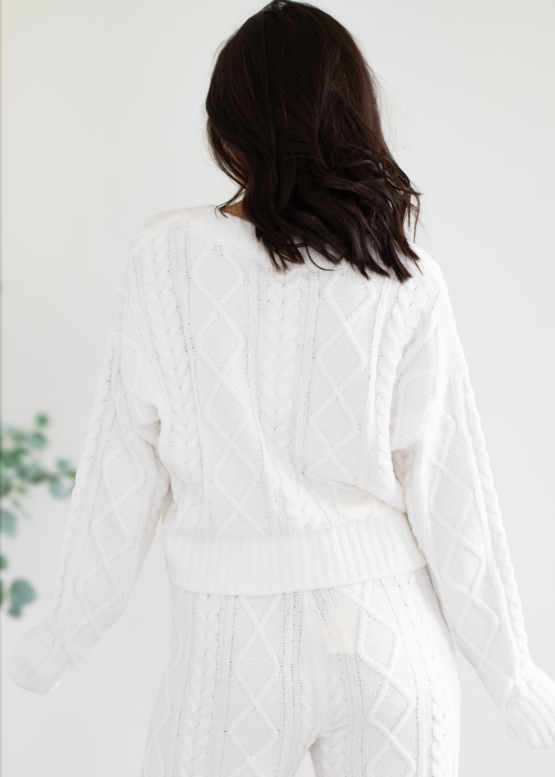 Person wearing a white cable knit cardigan against a plain background