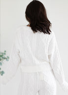 Person wearing a white cable knit cardigan against a plain background