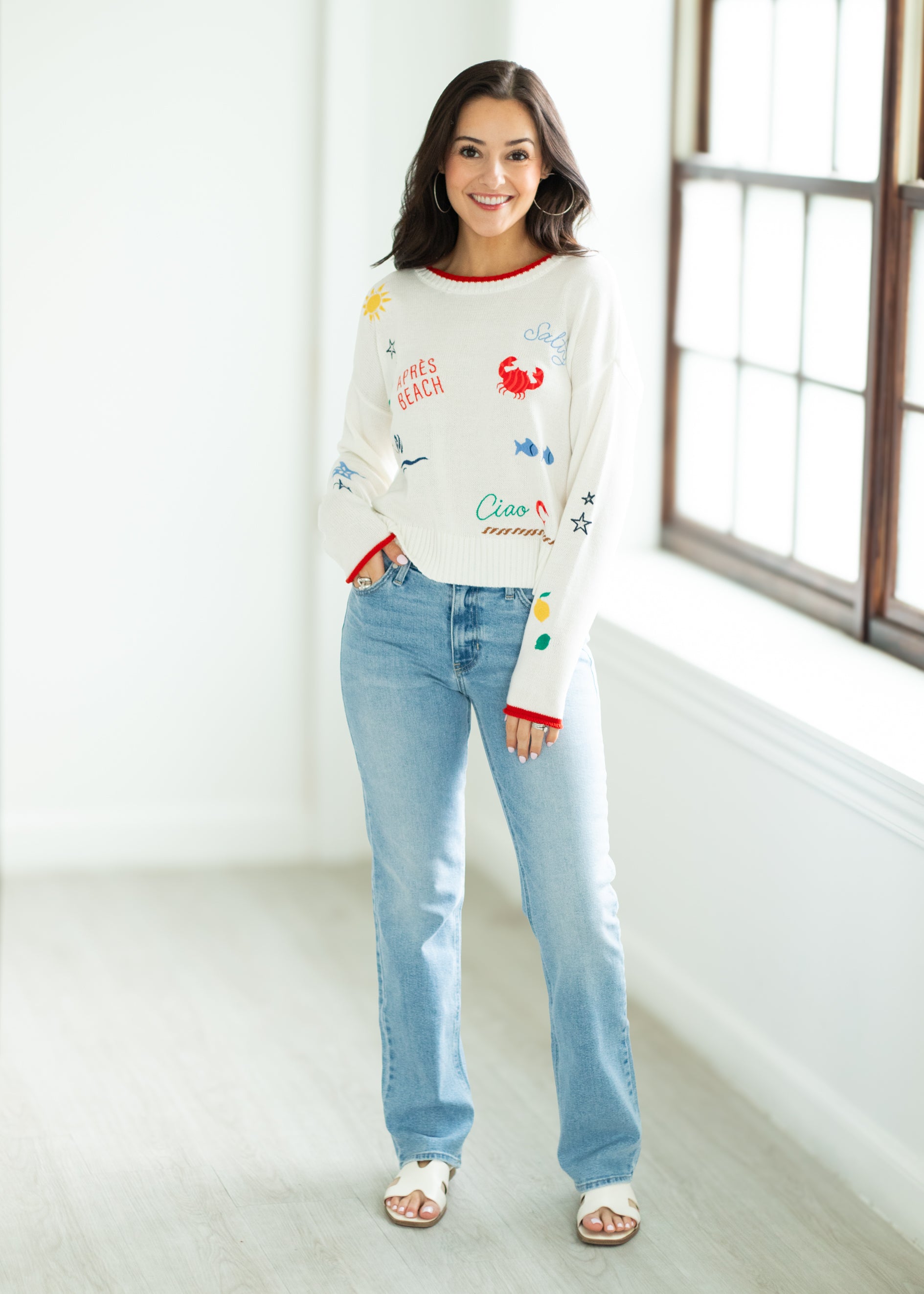 Woman wearing a colorful sweater and light blue jeans indoors.