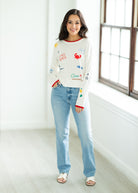 Woman wearing a colorful sweater and light blue jeans indoors.