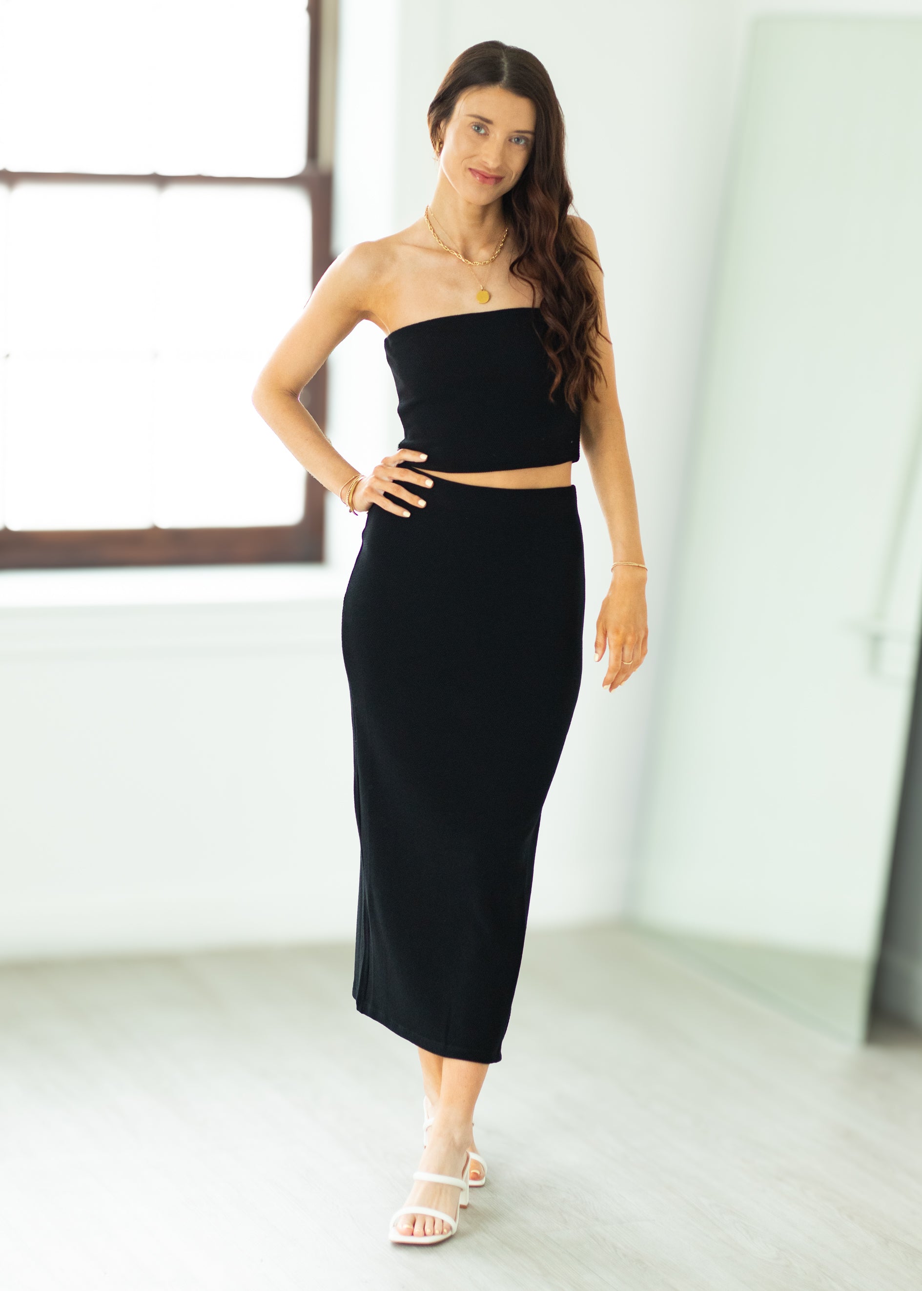 Woman wearing a black strapless top and high-waisted skirt in a minimalistic room.