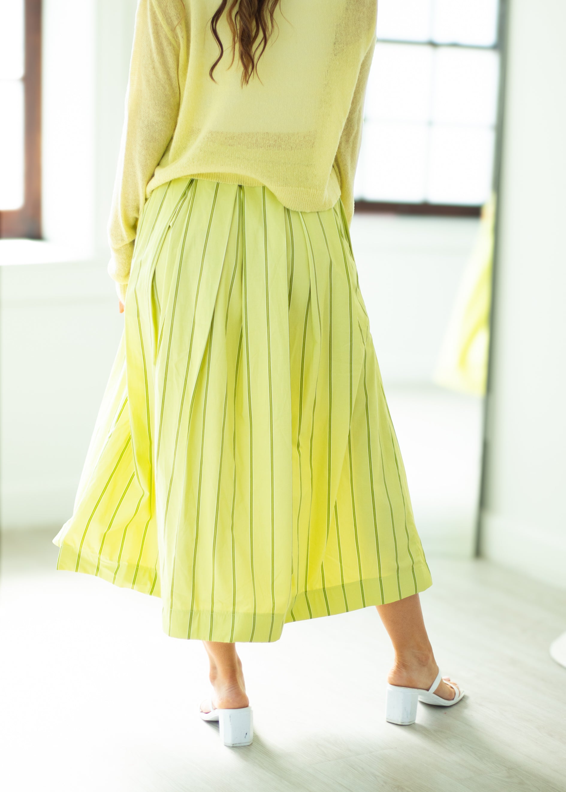Person wearing a yellow pleated skirt and top in a bright room.