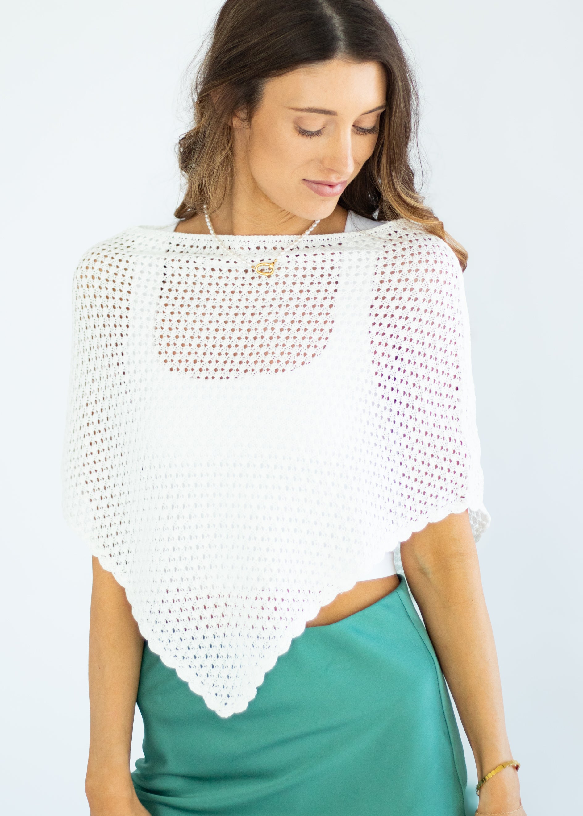 Woman wearing a white crochet shrug over a green dress on a light gray background