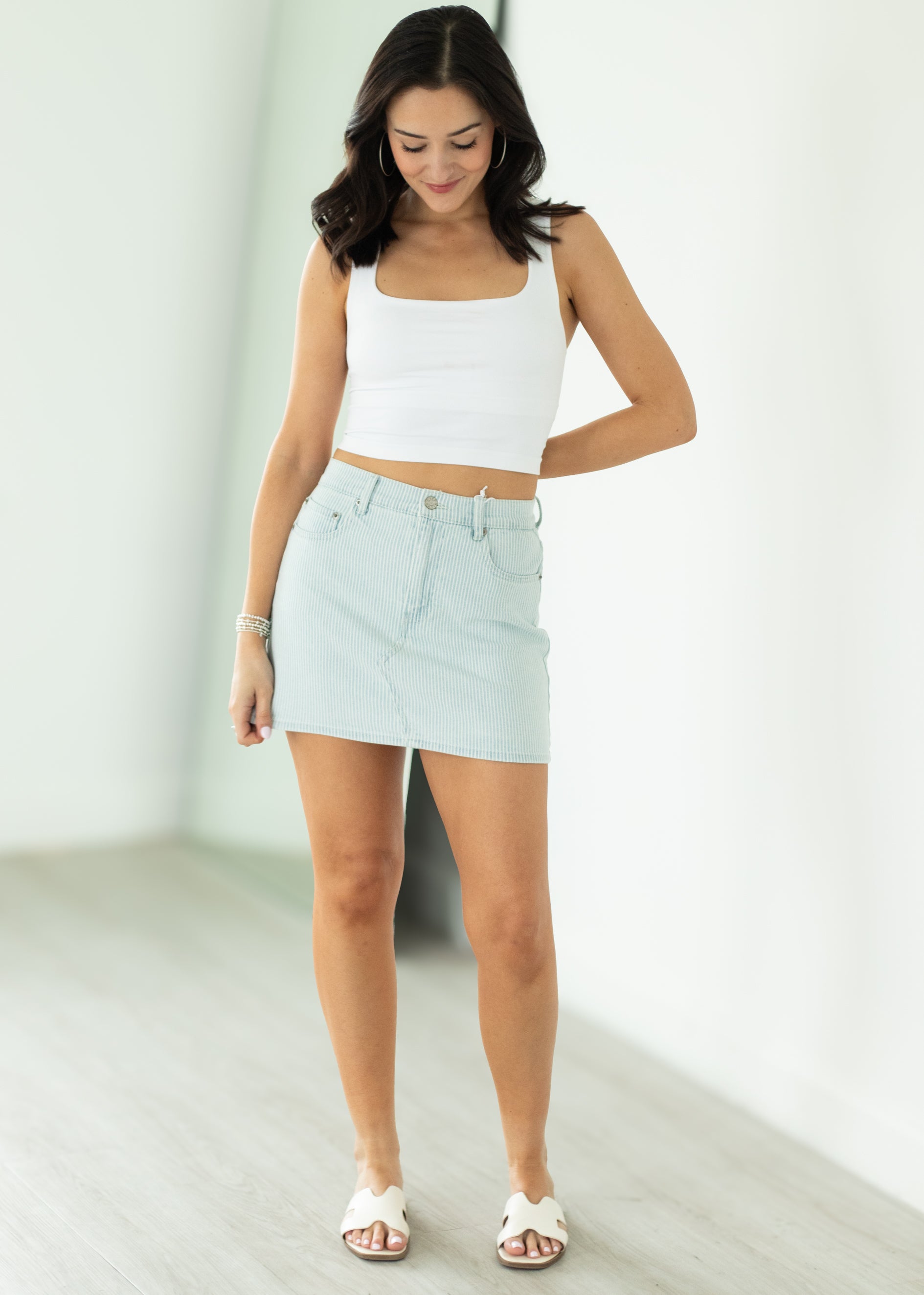 Woman wearing a white crop top and light blue denim skirt on a plain background