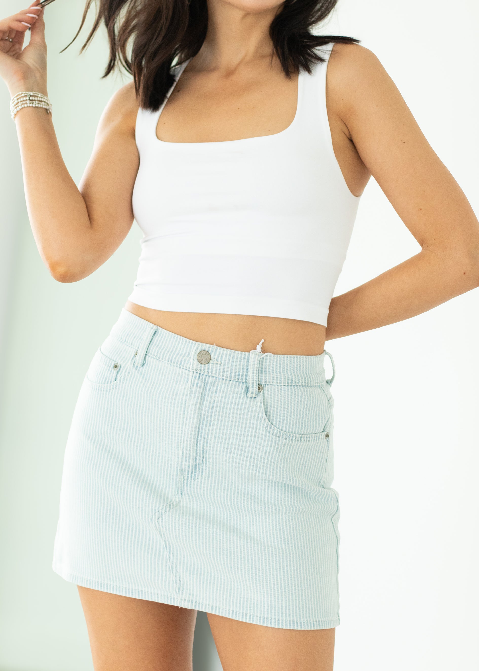 Woman wearing a white tank top and light blue checkered skirt on a plain background