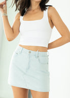 Woman wearing a white tank top and light blue checkered skirt on a plain background