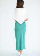 Woman wearing a white top and teal skirt on a white background