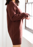 Person wearing a brown sweater in a bright room with a window.