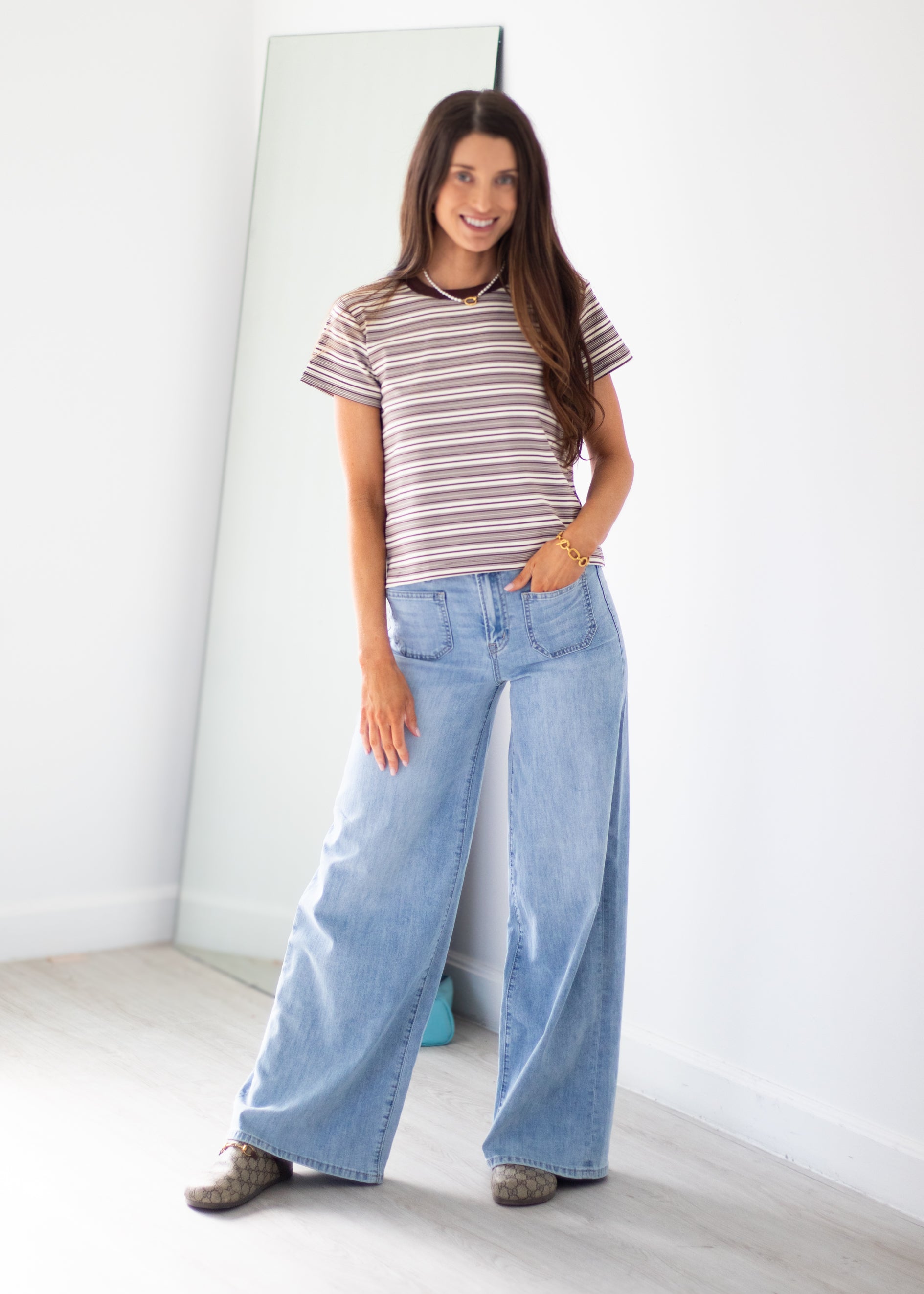 A woman modeling a short-sleeve striped t-shirt and wide-leg light blue jeans, standing in a bright room with a floor mirror.