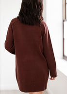 Person wearing a brown sweater dress against a white background