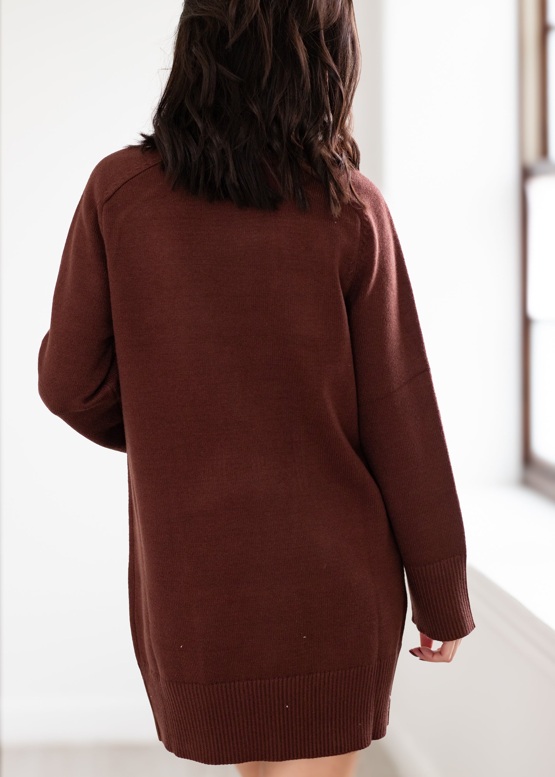 Person wearing a brown sweater dress against a white background