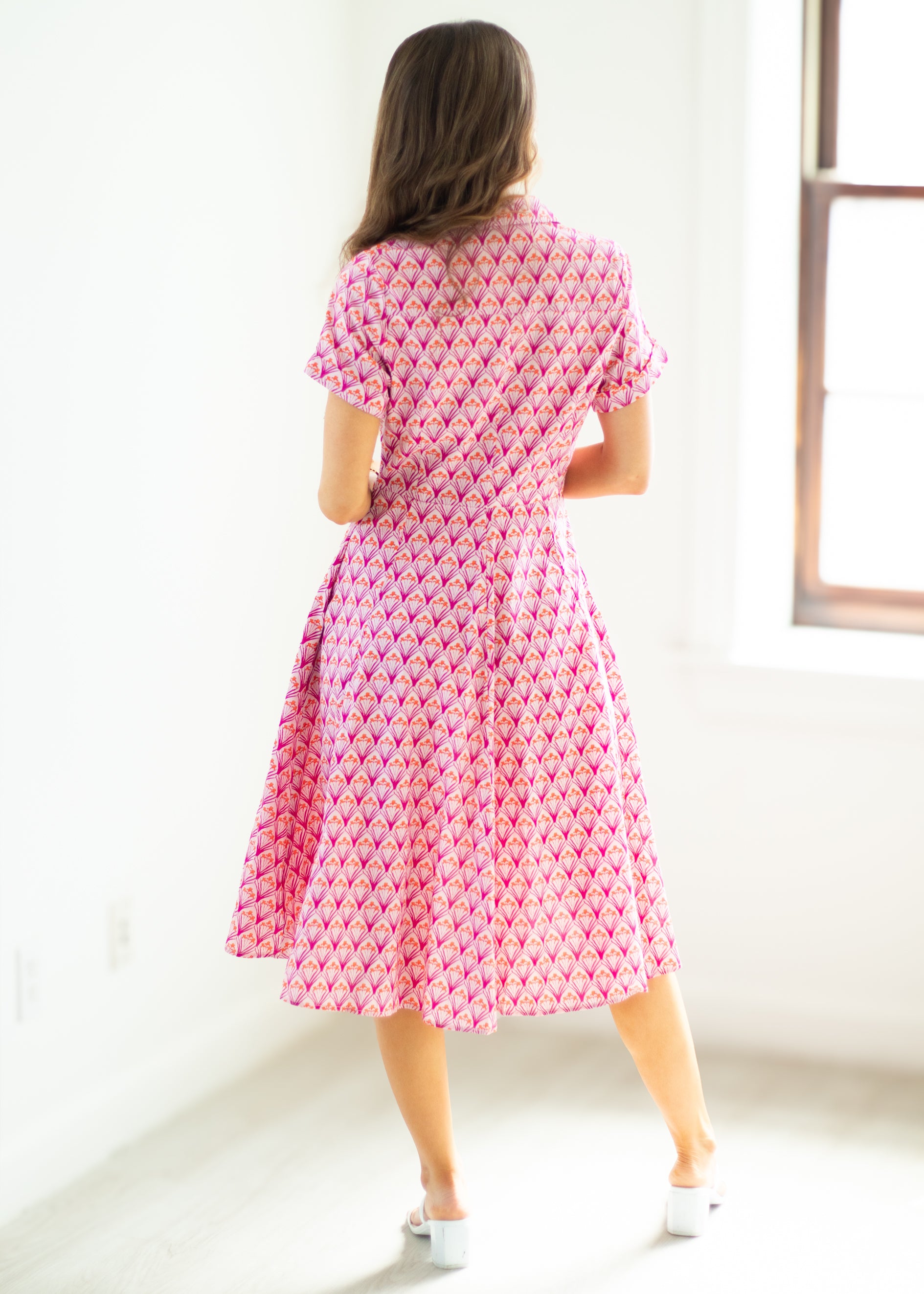 Woman wearing a pink patterned dress standing in a bright room.