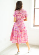 Woman wearing a pink patterned dress standing in a bright room.