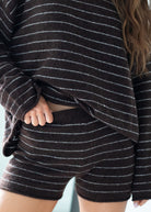 Close-up of a person wearing a dark brown fuzzy knit loungewear set with thin white horizontal stripes, including a cropped long-sleeve top and matching shorts.