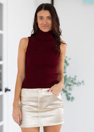 Woman wearing a burgundy sleeveless top and gold skirt indoors.