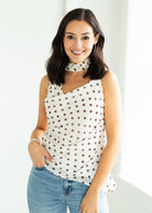 Woman wearing a white sleeveless top with brown polka dots and blue jeans against a white background