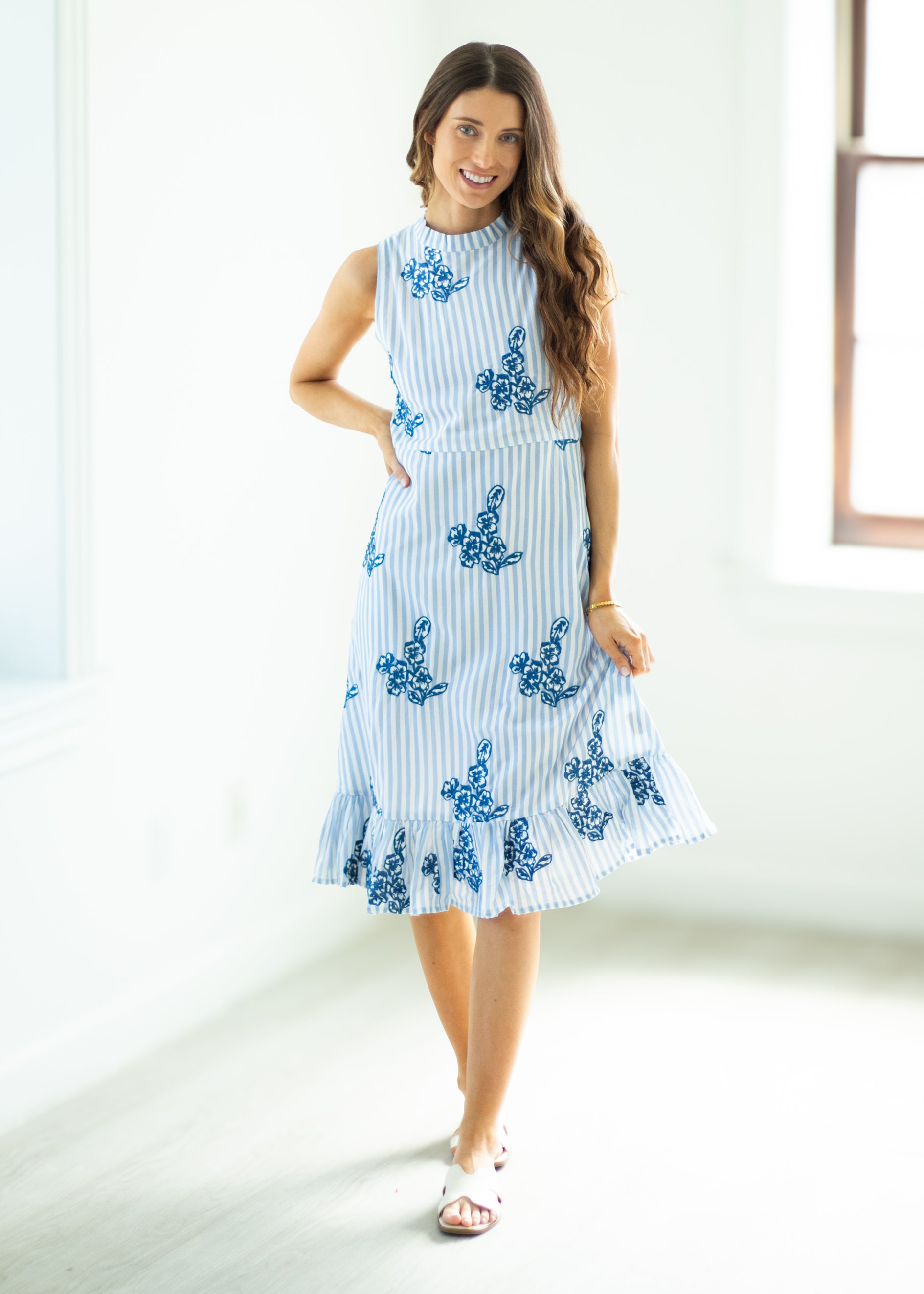 Woman wearing a blue and white dress with floral patterns in a bright room.