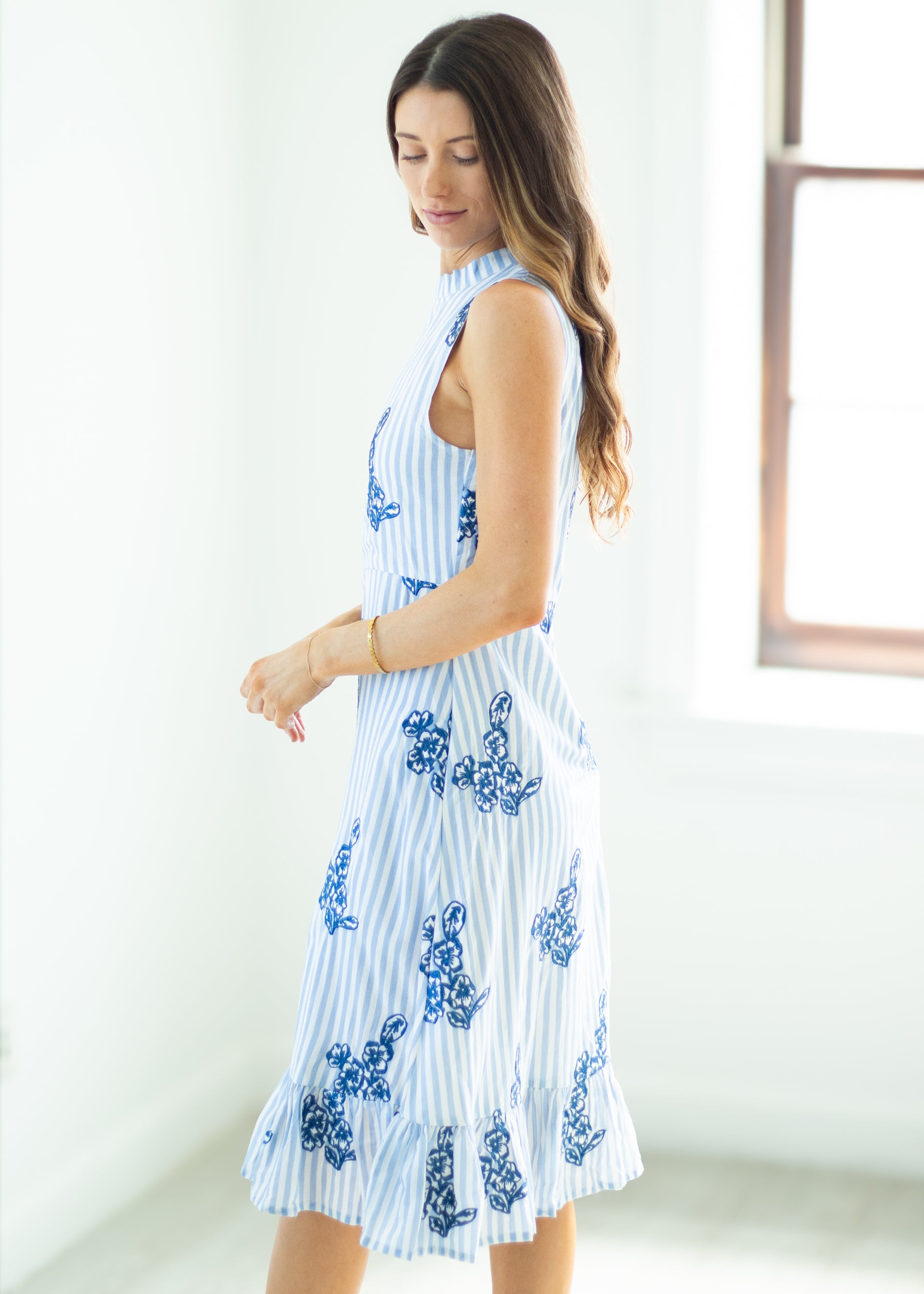 Woman wearing a white dress with blue floral patterns in a minimal indoor setting