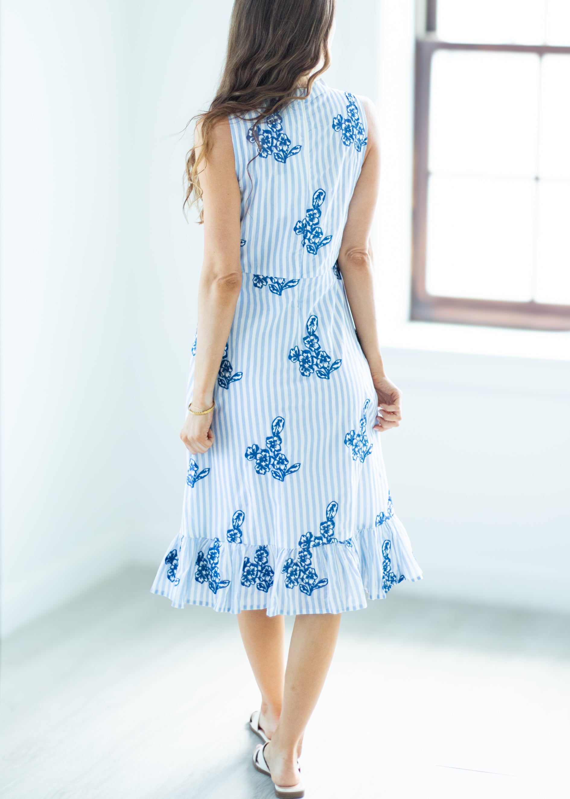 Woman wearing a white dress with blue floral patterns in a minimalistic setting.