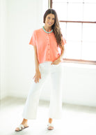Woman wearing a coral blouse and white pants in a bright room.