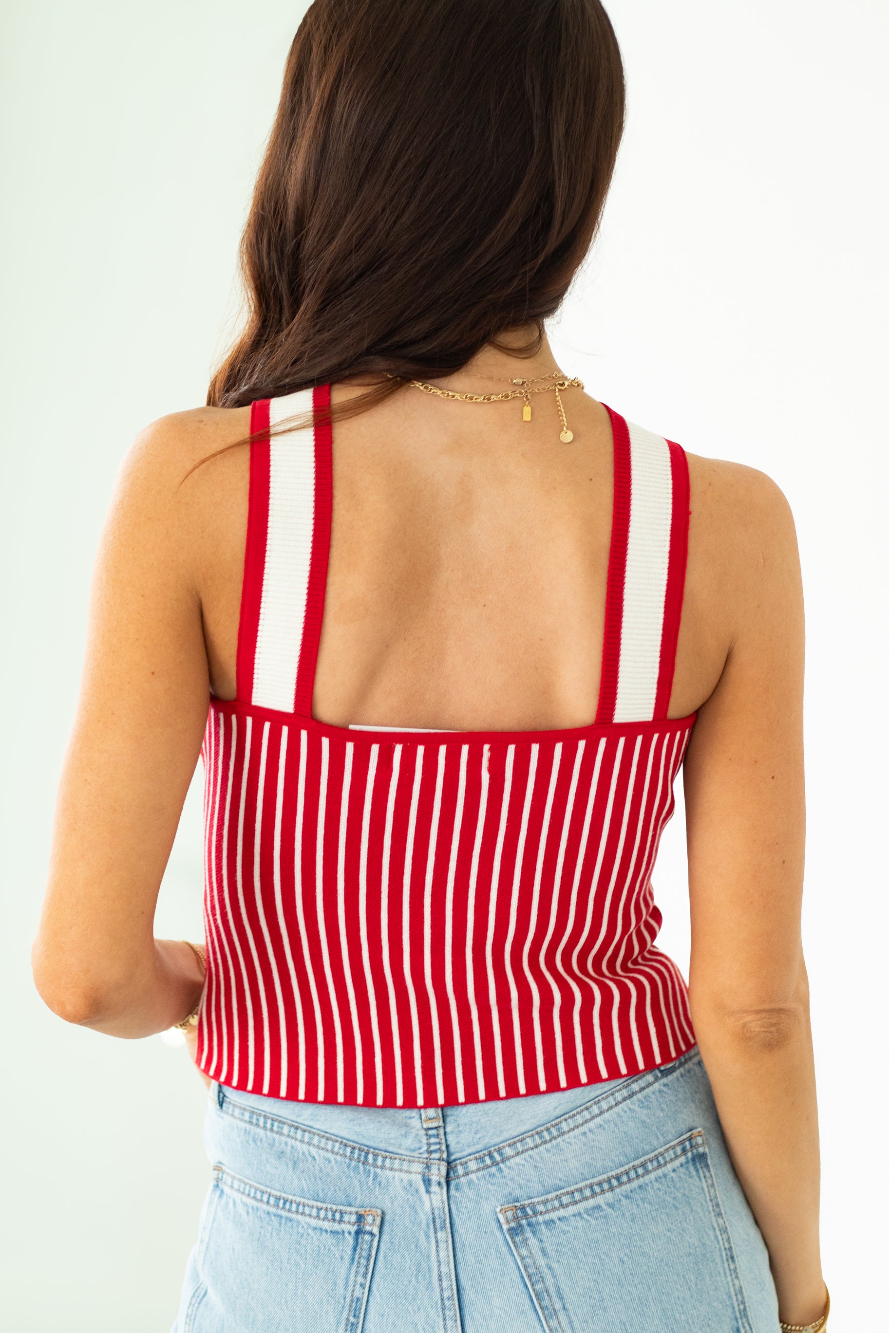 Woman wearing a red and white striped tank top with light blue jeans on a plain background