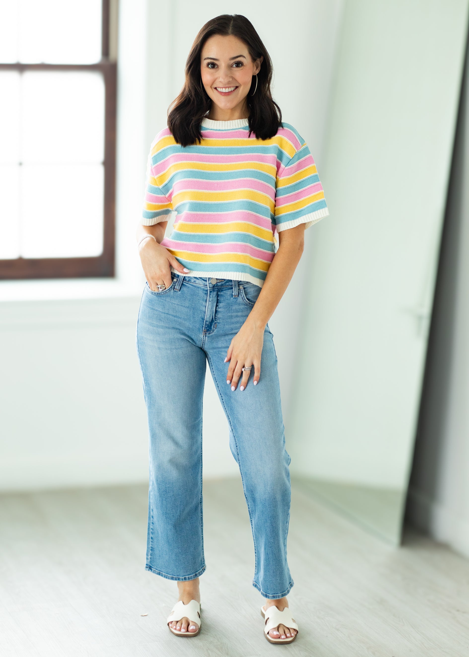 Woman wearing a colorful striped shirt and blue jeans indoors.