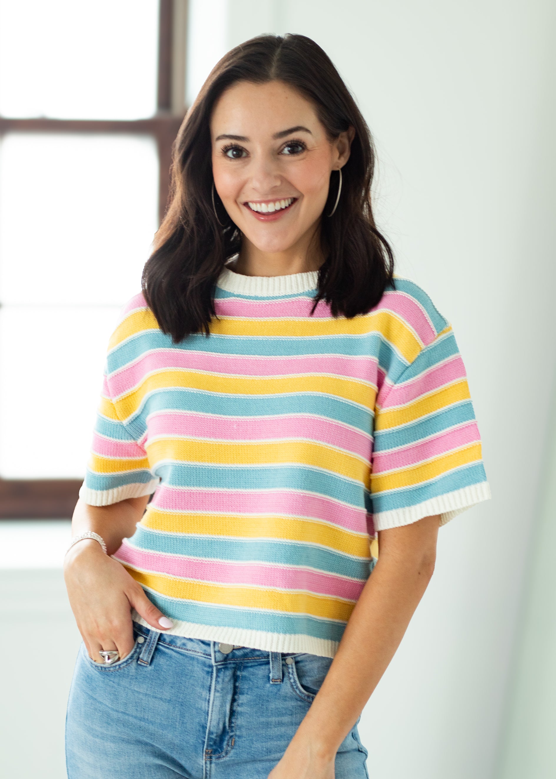 Woman wearing a colorful striped sweater and jeans indoors.