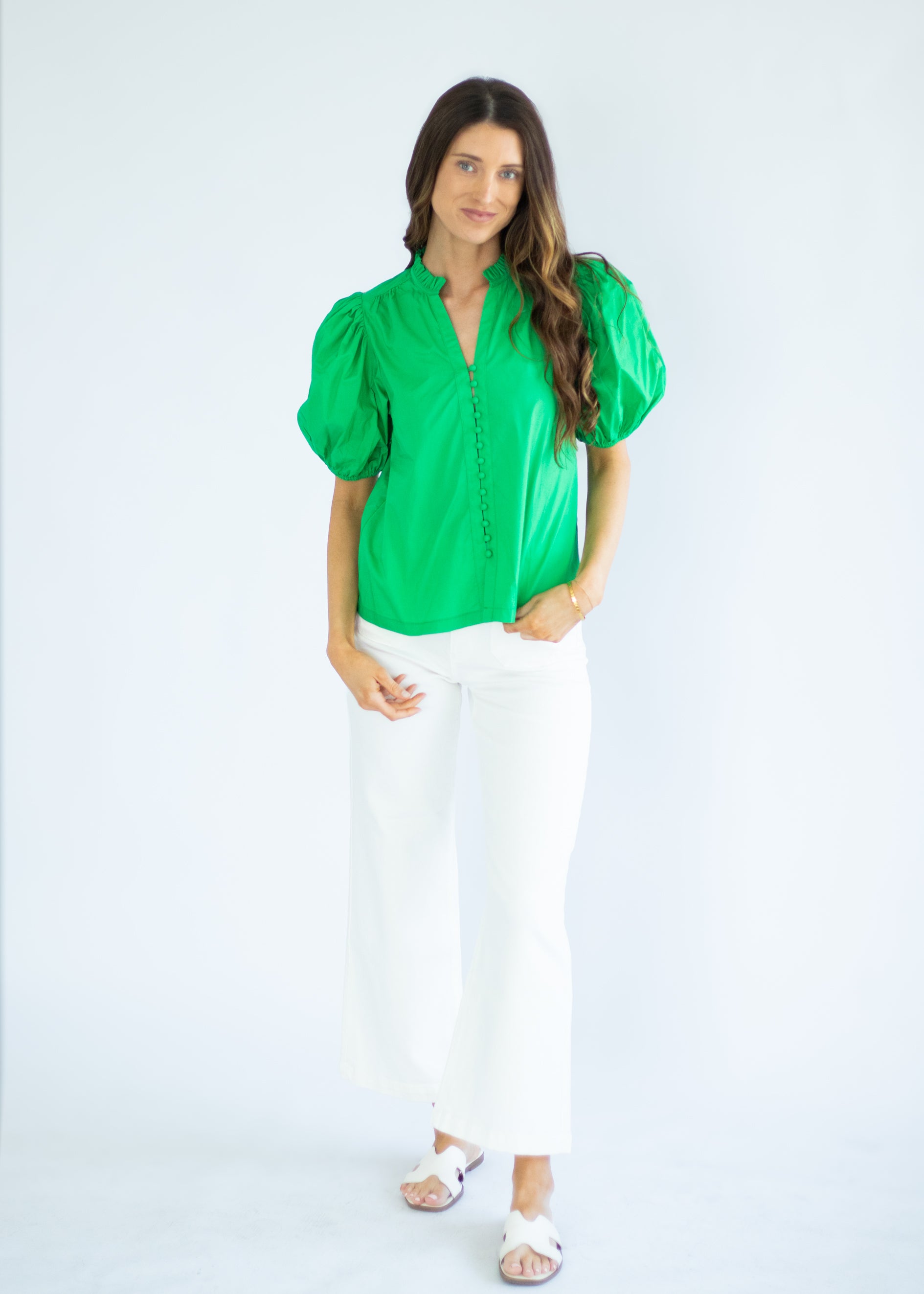 Woman wearing a green blouse and white pants on a white background