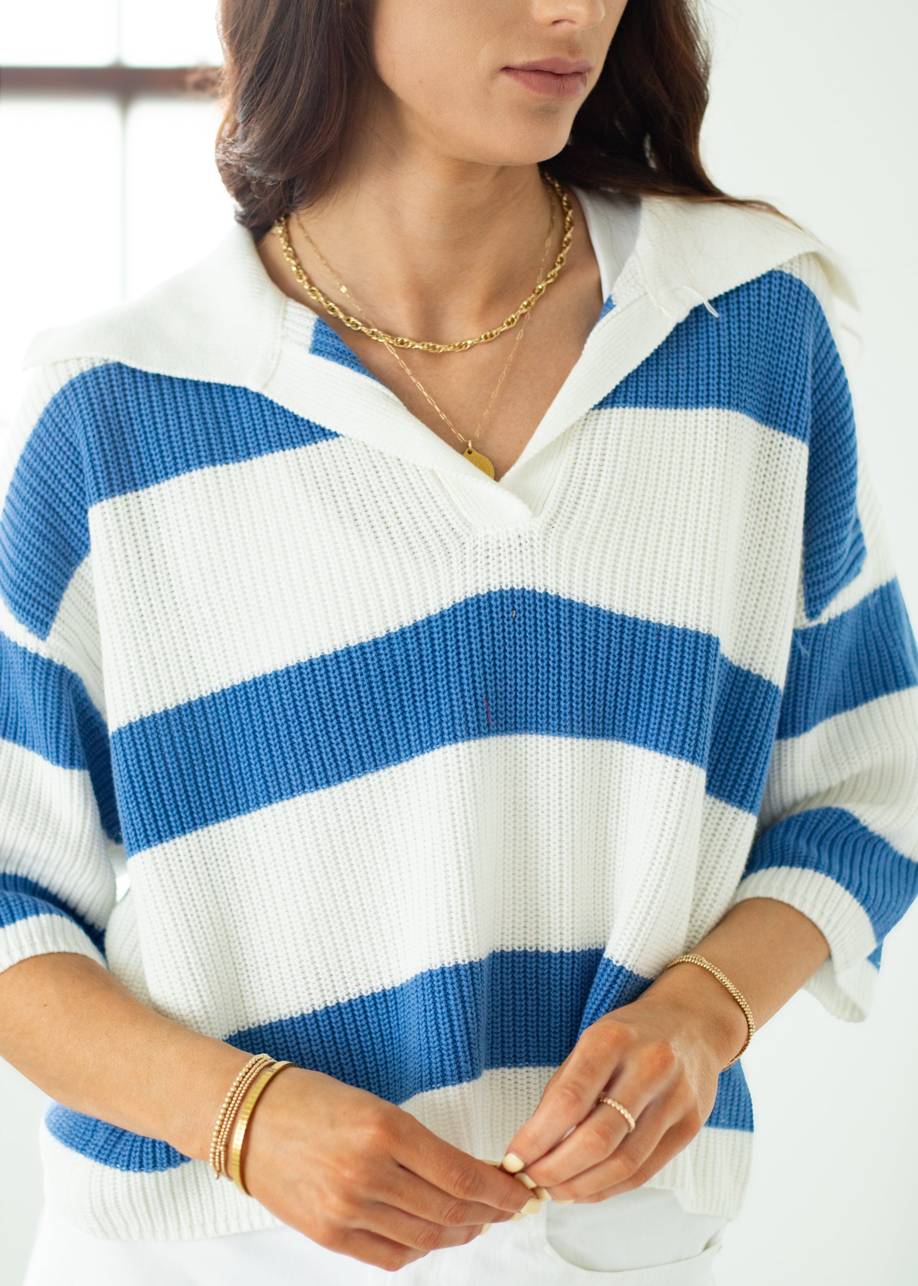 Person wearing a blue and white striped sweater with gold jewelry.