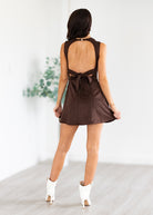 Woman wearing a brown dress with a bow detail, standing against a white background.