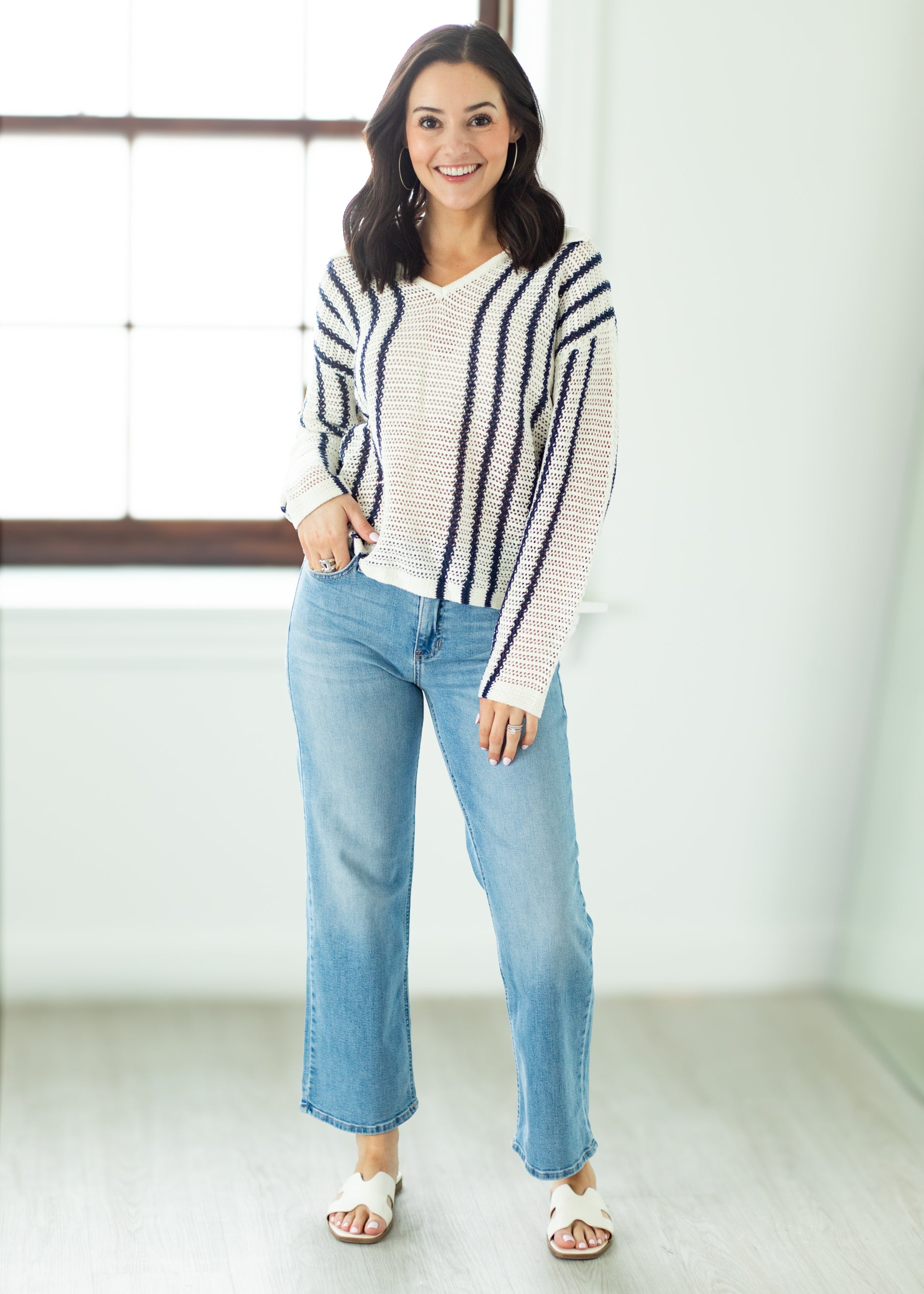 Woman wearing a striped sweater and blue jeans standing indoors.