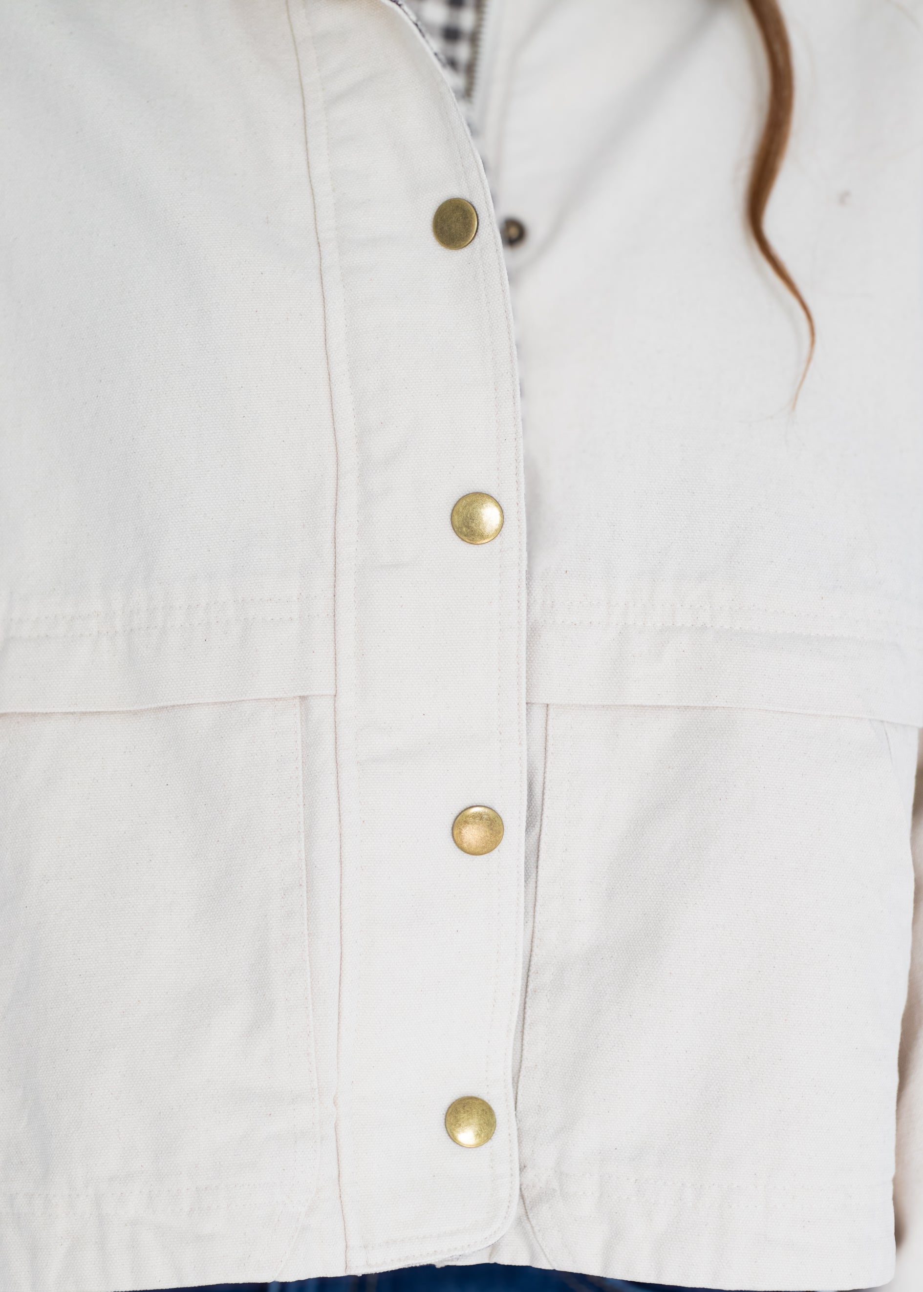 Close-up of a white or off-white jacket with gold-tone snap buttons and a small plaid lining visible at the collar.