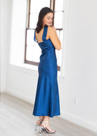 Woman wearing a blue dress in a bright room with large windows.