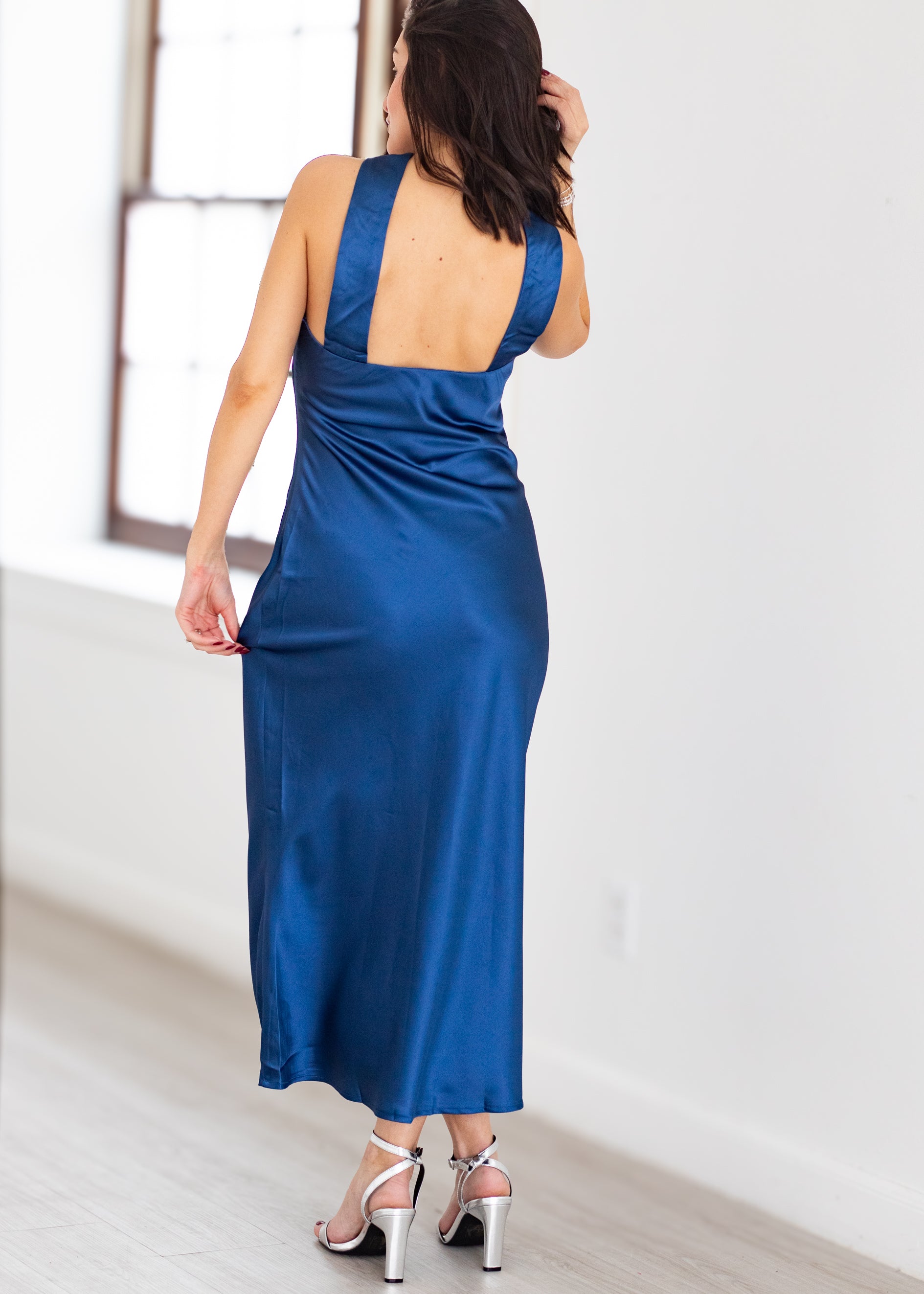 Woman wearing a blue satin dress with a backless design, standing in a minimalistic room.