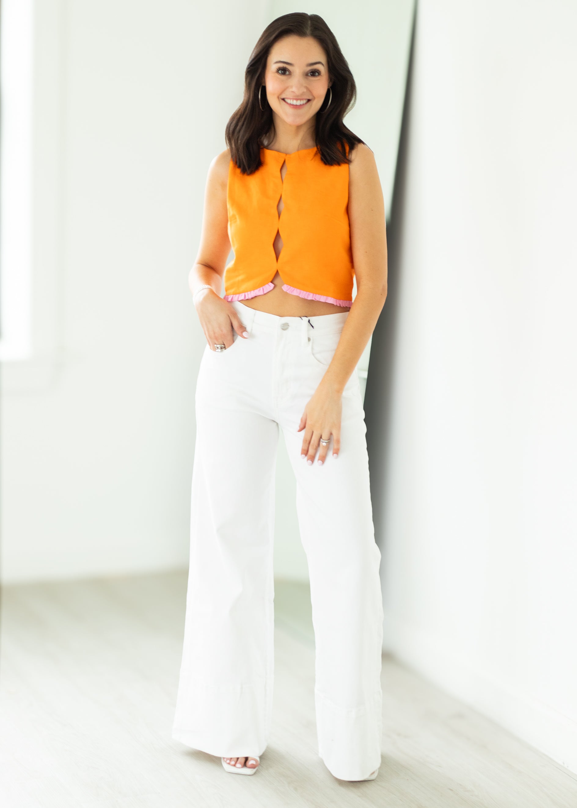 Woman wearing an orange top and white pants against a white background