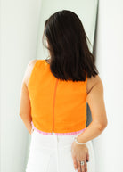 Woman wearing an orange sleeveless top with a white background