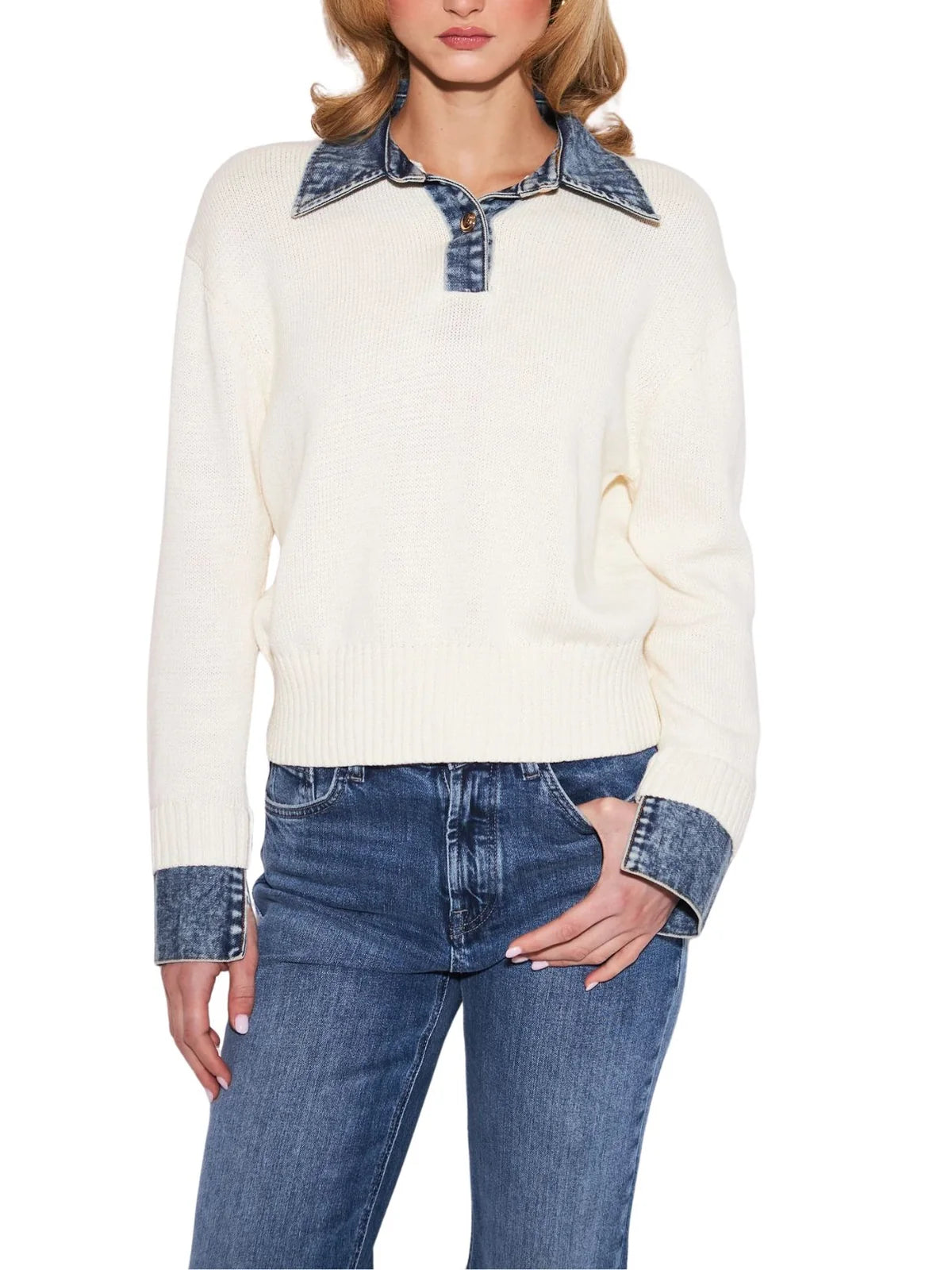 A woman wearing a cream ribbed knit sweater with contrasting blue denim collar and cuffs, paired with blue jeans, against a plain white background.