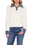 A woman wearing a cream ribbed knit sweater with contrasting blue denim collar and cuffs, paired with blue jeans, against a plain white background.