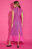 A woman modeling a bright pink sleeveless lace midi dress from the back, standing against a solid pink studio backdrop.