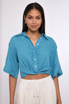 Woman wearing a blue cropped shirt and white pants on a white background