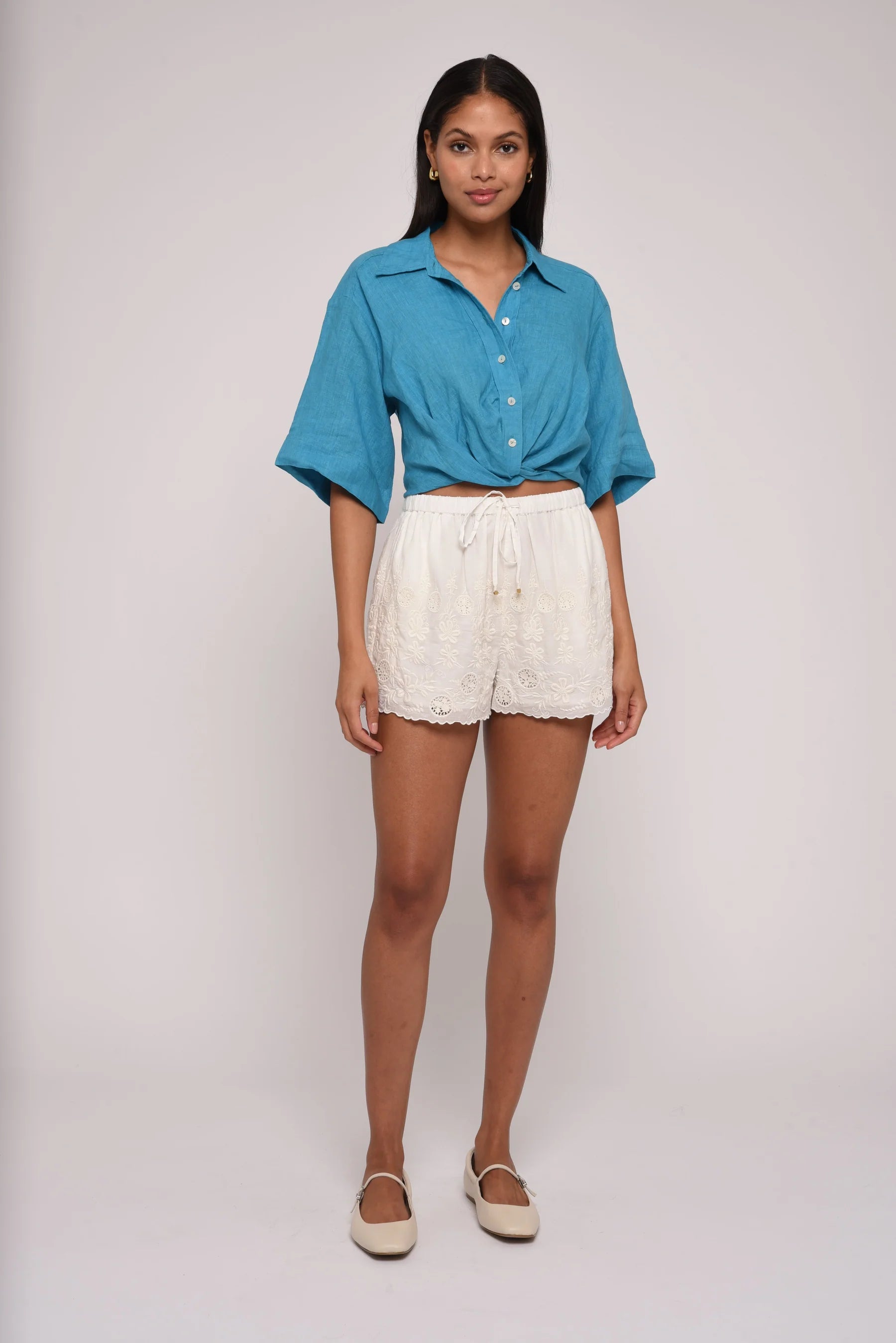 Woman wearing a blue shirt and white shorts on a plain background