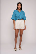 Woman wearing a blue shirt and white shorts on a plain background