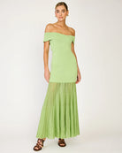 Woman wearing a light green off-shoulder dress with a sheer overlay on a white background